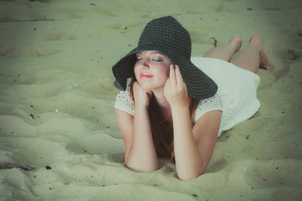 Rothaarige Frau mit Sonnenhut am Strand liegend — Stockfoto