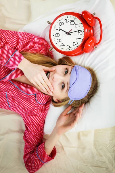 Sömnig kvinna klädd i pyjamas håller klockan — Stockfoto