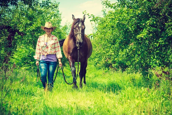 西方女人走在绿色的草原上，与马 — 图库照片