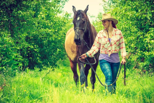 Западная женщина ходит по зеленому лугу с лошадью — стоковое фото