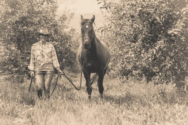 Western woman walking on green meadow with horse — Stock Photo, Image