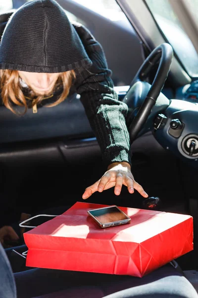 Burglar thief stealing smartphone and bag from car — Stock Photo, Image