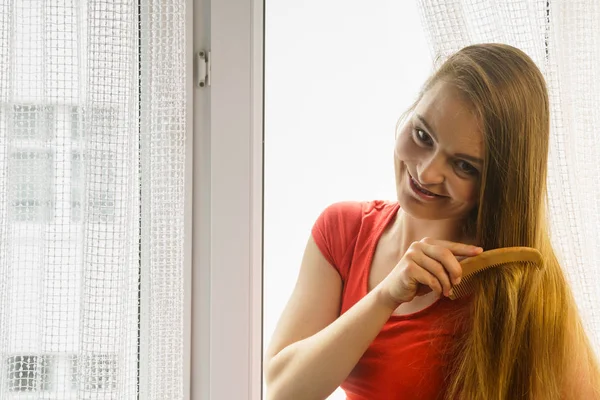 Kvinna som sitter på fönsterkarm borsta håret — Stockfoto