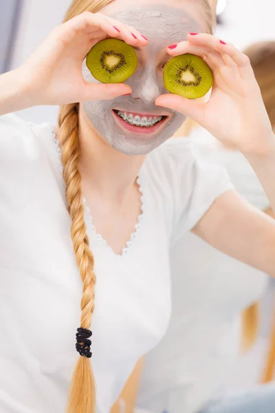 Jovem feliz tendo máscara facial segurando kiwi — Fotografia de Stock