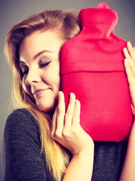 Woman hugs hot water bottle in red fleece cover — Stock Photo, Image