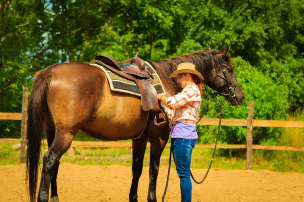 Cowgirl getting horse ready for ride on countryside — Stock Photo, Image