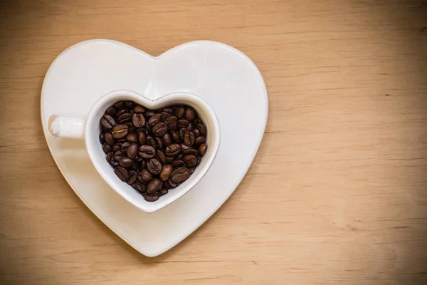 Tazza a forma di cuore con chicchi di caffè sul tavolo di legno — Foto Stock