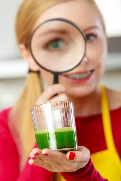 Woman looking at vegetable juice through magnifying glass — Stock Photo, Image