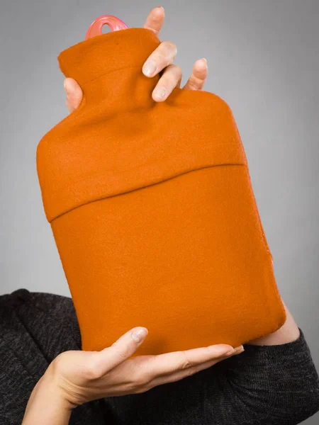 Kvinna som håller varm orange varmvattenflaska — Stockfoto