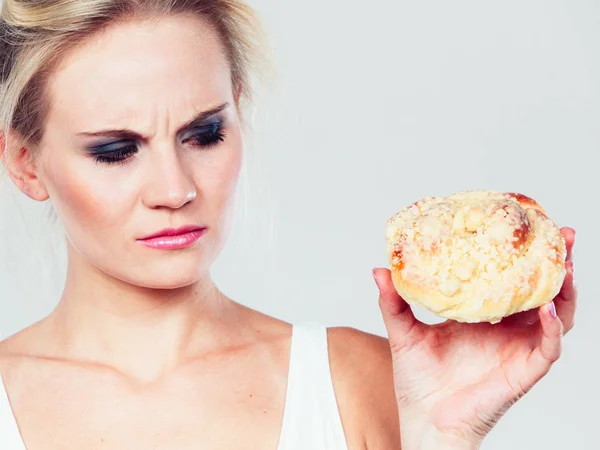 Undecided woman holds cake sweet bun in hand — Stock Photo, Image