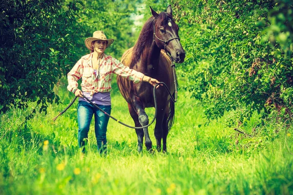 Mujer occidental caminando sobre prado verde con caballo — Foto de Stock