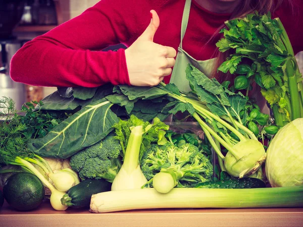 Kvinna i köket med många gröna grönsaker — Stockfoto
