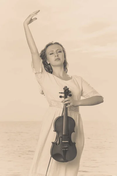 Donna sulla spiaggia vicino al mare che tiene violino — Foto Stock