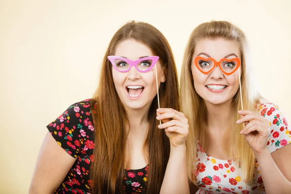 Dos mujeres felices sosteniendo anteojos falsos en palo — Foto de Stock
