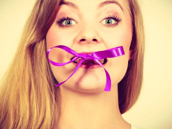 Blonde woman biting decorative purple bow — Stock Photo, Image