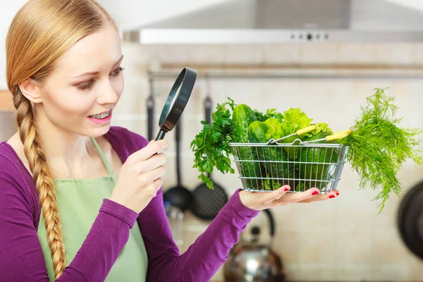 Mujer mirando a través de la lupa en la cesta de verduras — Foto de Stock