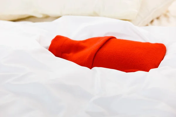 Warm red hot water bottle on white bedding — Stock Photo, Image