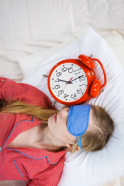 Sleeping woman wearing pajamas holding clock — Stock Photo, Image