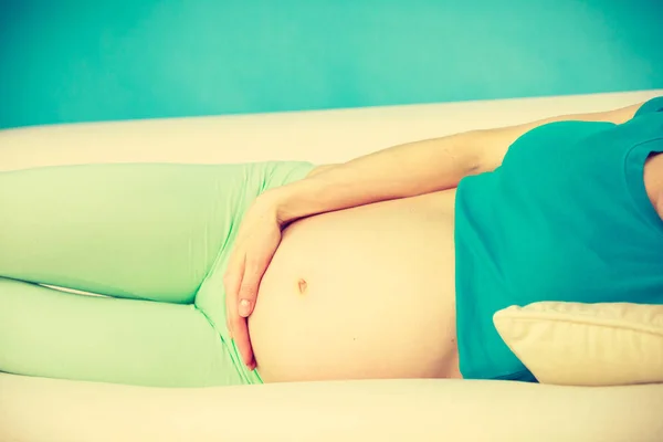 Femme enceinte couchée sur le canapé touchant son ventre — Photo