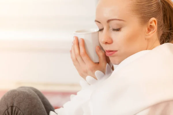 Mujer acostada en un sofá bajo una manta bebiendo té —  Fotos de Stock