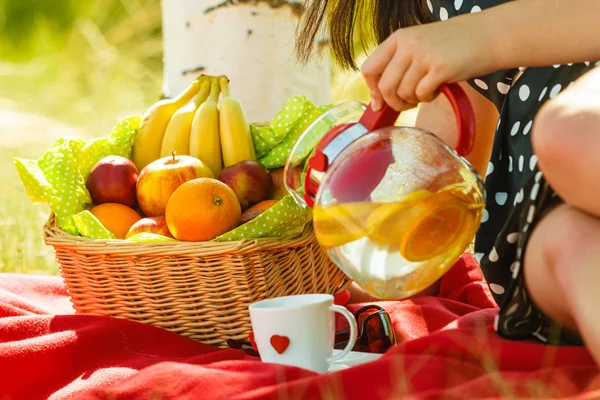 Picnic basket on blanket, woman pouring water into cup — Stock Photo, Image