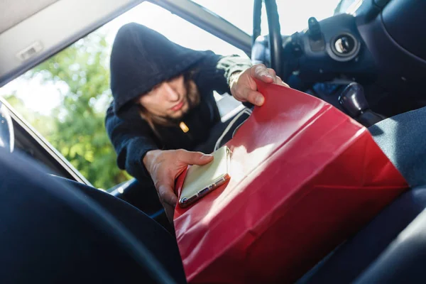 Burglar thief stealing smartphone and bag from car — Stock Photo, Image