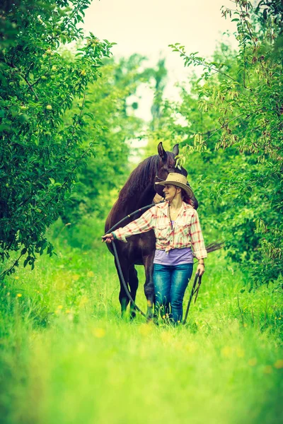 Westerse vrouw lopen op groene weide met paard — Stockfoto