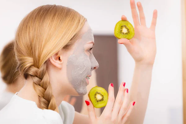 Gelukkig jonge vrouw met gezicht masker bedrijf kiwi — Stockfoto