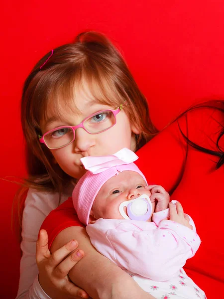 Toddler girl kissing newborn sister held by mother — Stock Photo, Image