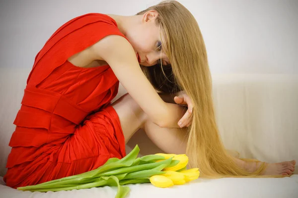 Triste femme élégante assise sur un canapé avec tulipe — Photo