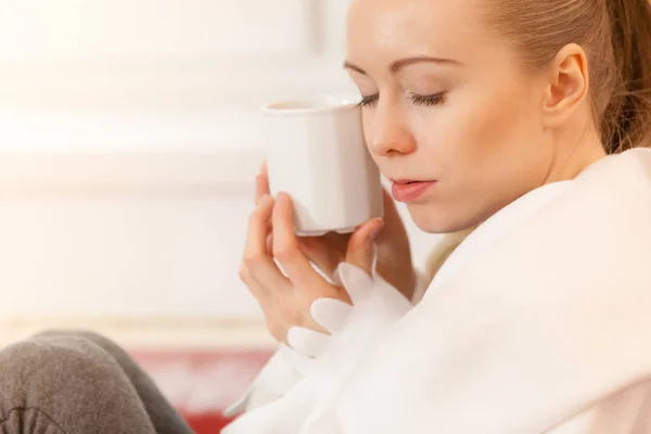 Mujer acostada en un sofá bajo una manta bebiendo té —  Fotos de Stock