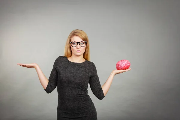 Woman in eyeglasses being confused holding brain — Stock Photo, Image