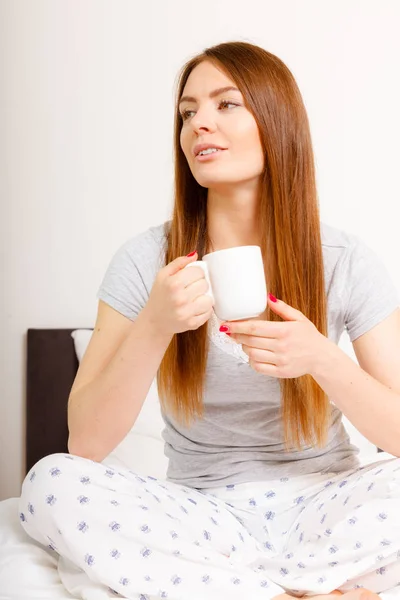 Smiling woman holding cup of drink in bed — Stock Photo, Image