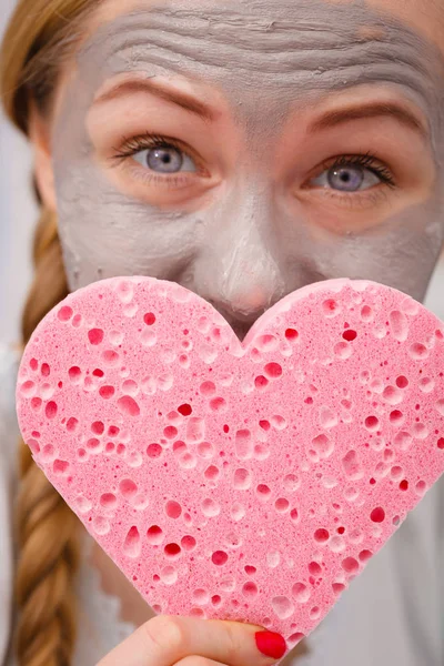 Woman having grey face mask holding heart sponge — Stock Photo, Image