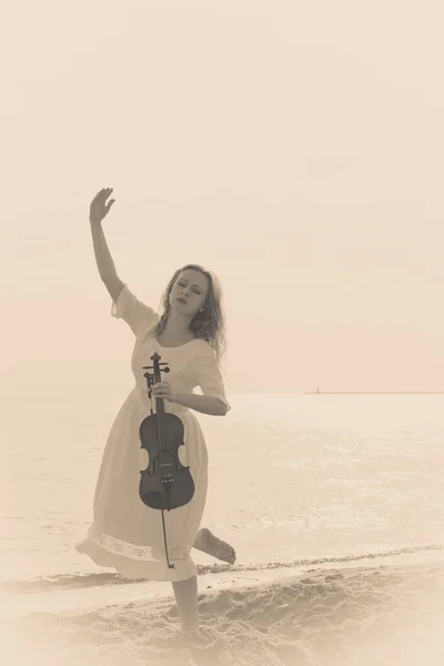 Kvinna på stranden nära havet håller fiol — Stockfoto