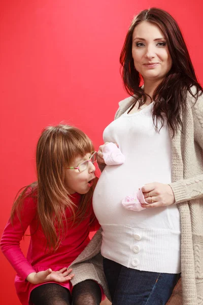 Mujer embarazada con niña pequeña sosteniendo zapatos de bebé — Foto de Stock