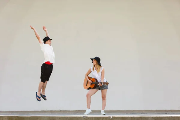Женщина играет на гитаре, мужчина прыгает рядом с ней — стоковое фото