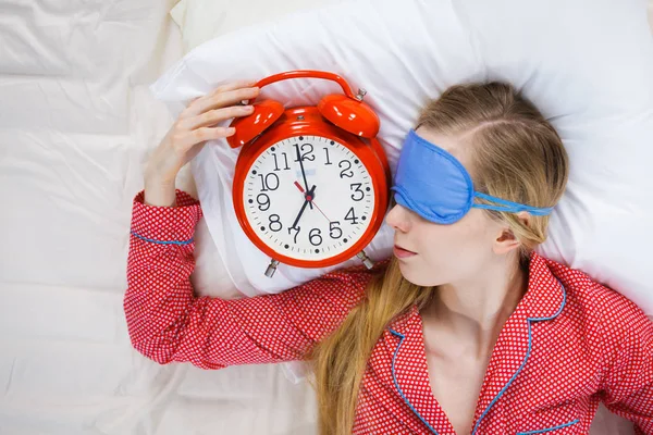 Schlafende Frau im Schlafanzug hält Uhr — Stockfoto