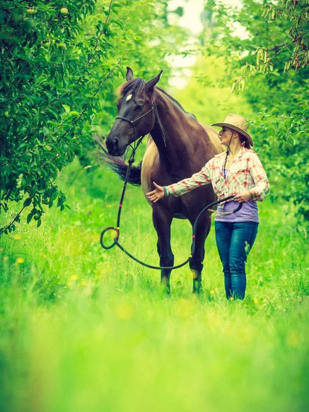 Westerse vrouw lopen op groene weide met paard — Stockfoto