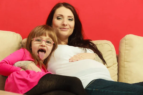 Mujer embarazada sentada en el sofá con su hija —  Fotos de Stock