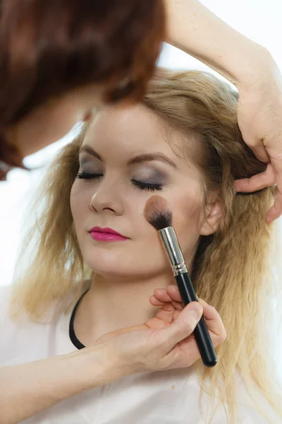 Artista de maquillaje aplicando con cepillo rouge en cheque femenino —  Fotos de Stock