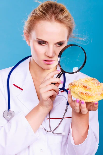 Doctor with magnifying glass examining sweet food — Stock Photo, Image