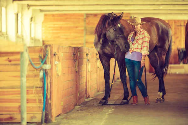 Cowgirl a žokej procházky s koňmi ve stáji — Stock fotografie