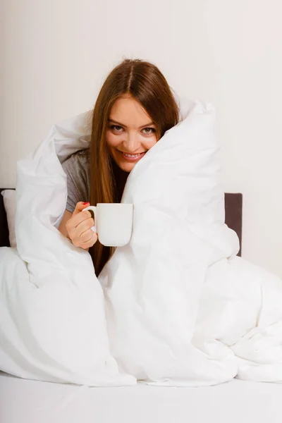 Улыбающаяся женщина с чашкой напитка в постели — стоковое фото