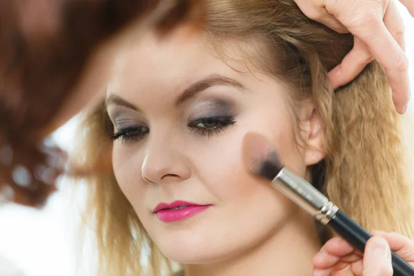 Maquiagem artista aplicando com escova rouge no cheque feminino — Fotografia de Stock