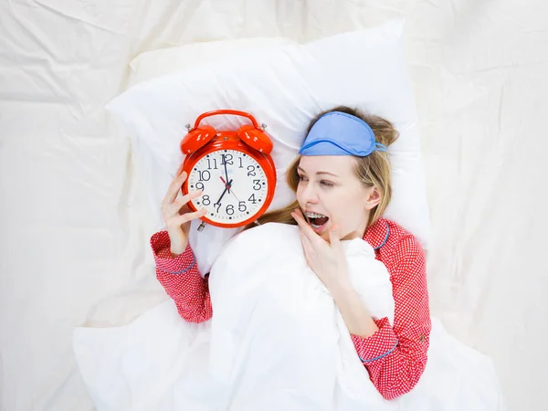 Shocked woman wearing pajamas holding clock overslept — Stock Photo, Image