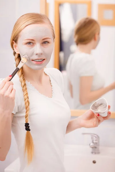 Frau trägt mit Pinsel Lehmmaske auf ihr Gesicht auf — Stockfoto