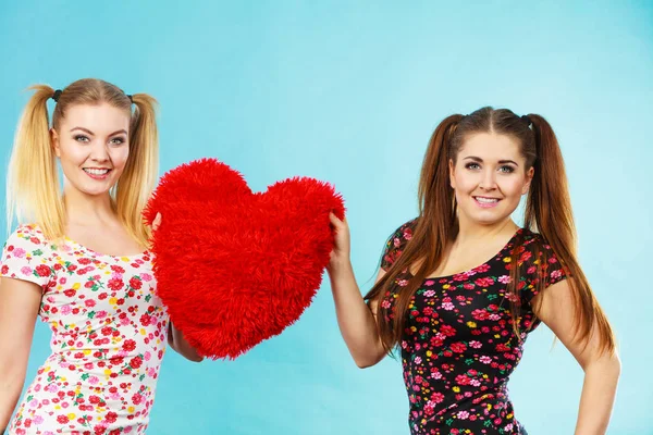 Feliz dos mujeres sosteniendo almohada en forma de corazón —  Fotos de Stock