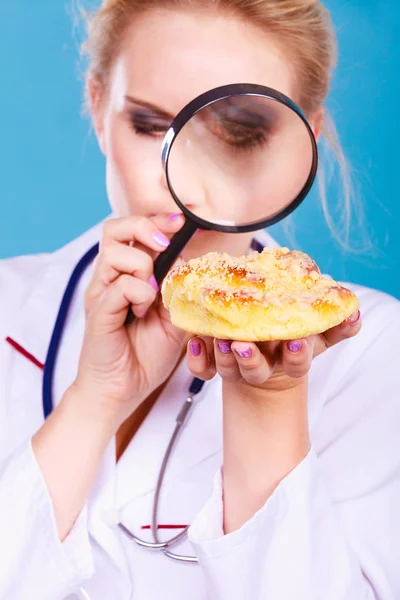 Doctor with magnifying glass examining sweet food — Stock Photo, Image