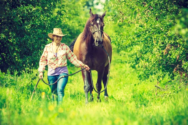 Mujer occidental caminando sobre prado verde con caballo —  Fotos de Stock